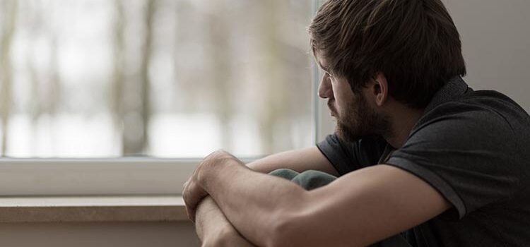 Junger Mann mit Burnout oder einer Depression schaut aus dem Fenster (Illustration: © Photographee.eu, Adobe Stock)